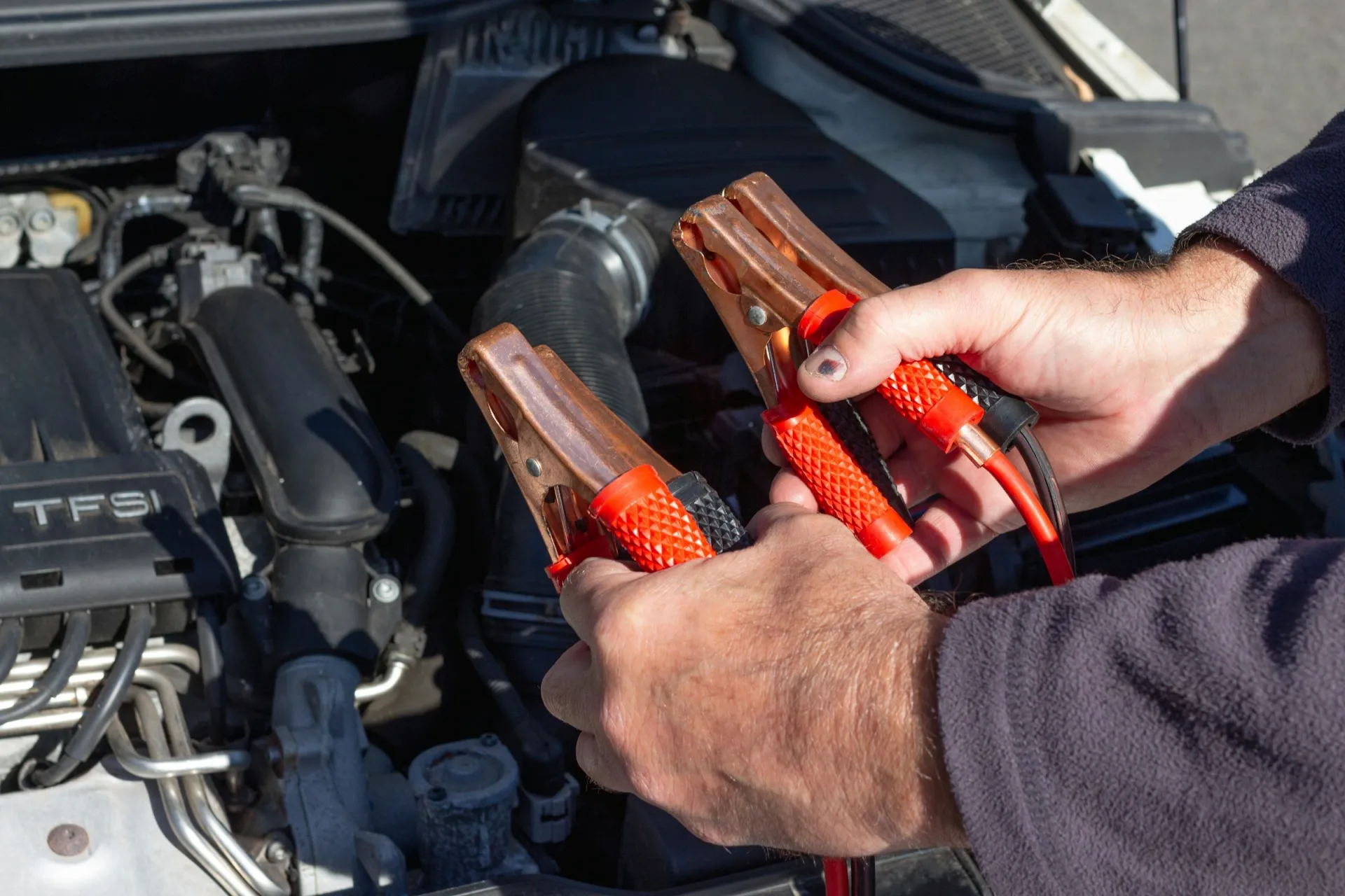 Technician holding jumper cable clamps over an engine