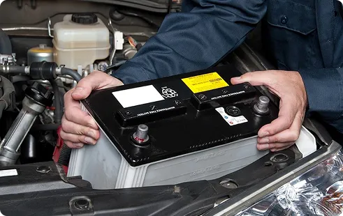 Technician lifting a car battery out of the engine bay