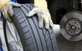 Gloved hands holding a car tire in the workshop